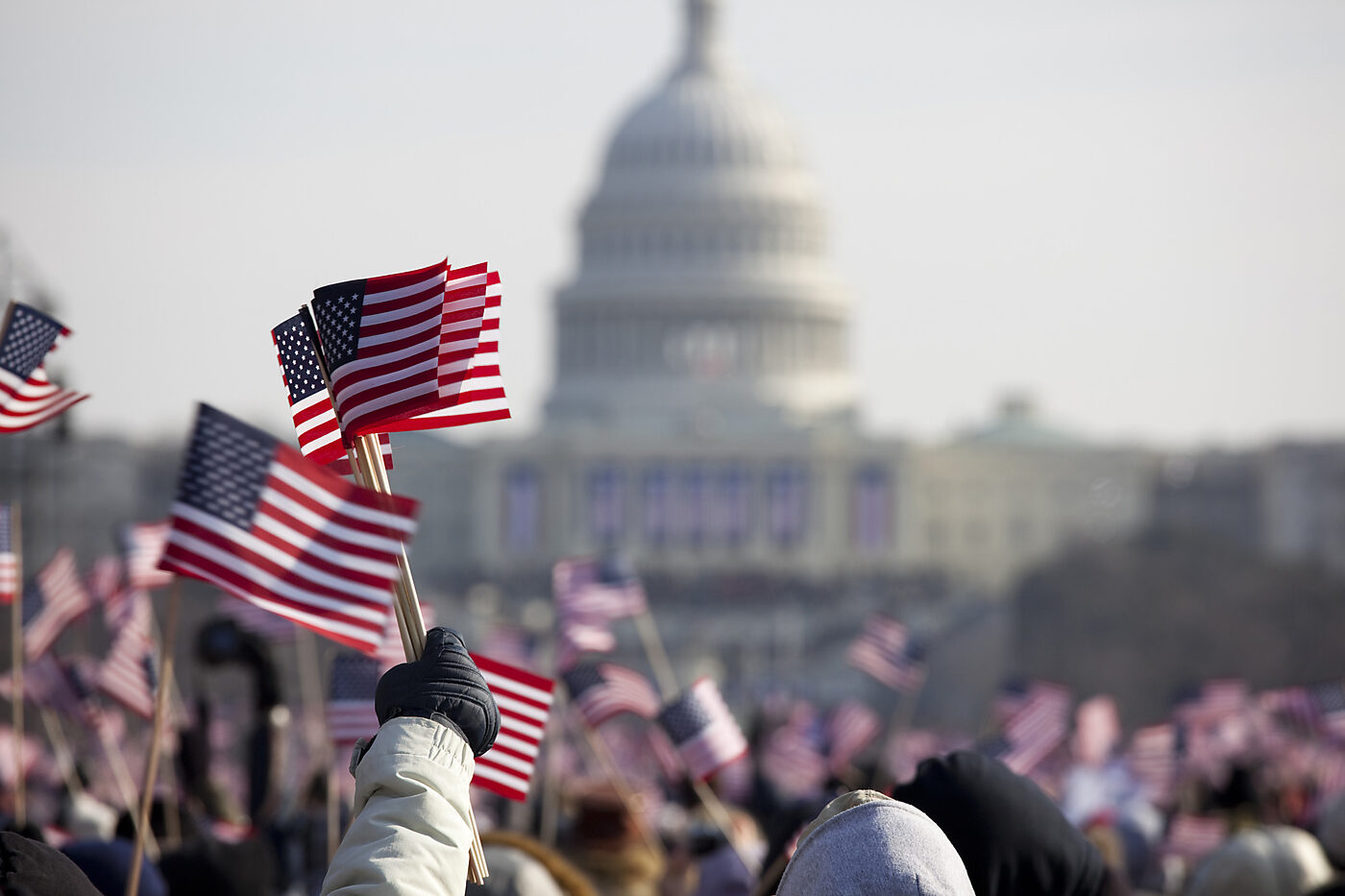 Crowd of people wave small American flags on the National Mall with the US Capitol in the background